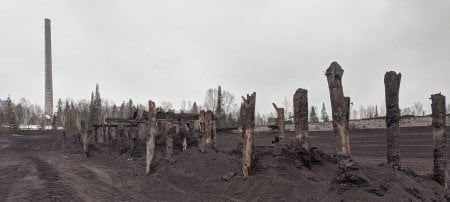 poles from an old sluiceway and a wooden road on black sand with a smokestack rising out of the sky behind it at the Gay sands