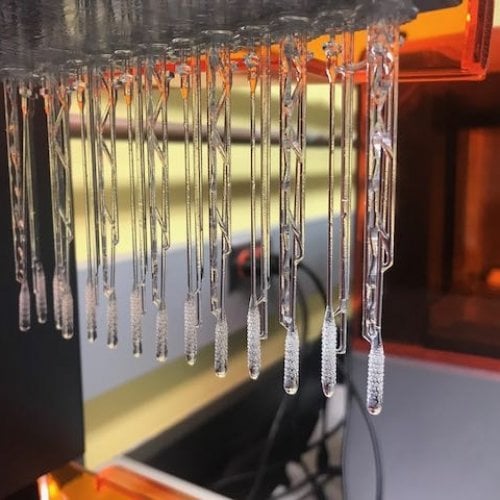 a row of clear plastic swabs emerge from a 3D printer