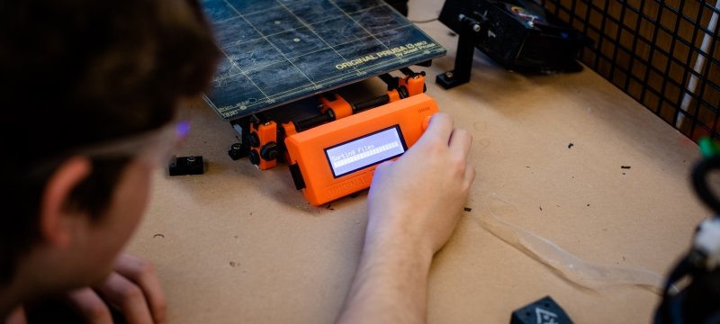 a student with safety glasses places his hand on test equipment with a digital readout in an open source laboratory on a college campus