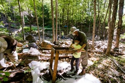 A man and a child work together with a sluice box at an archaeology site.