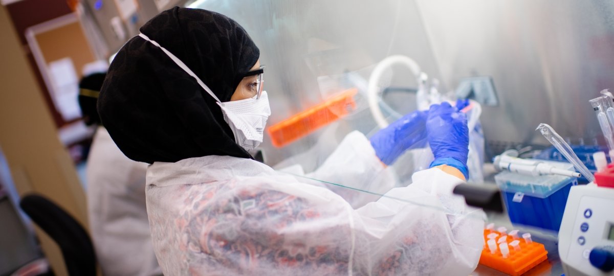 person in disposable PPE working in a lab with their hands under a hood