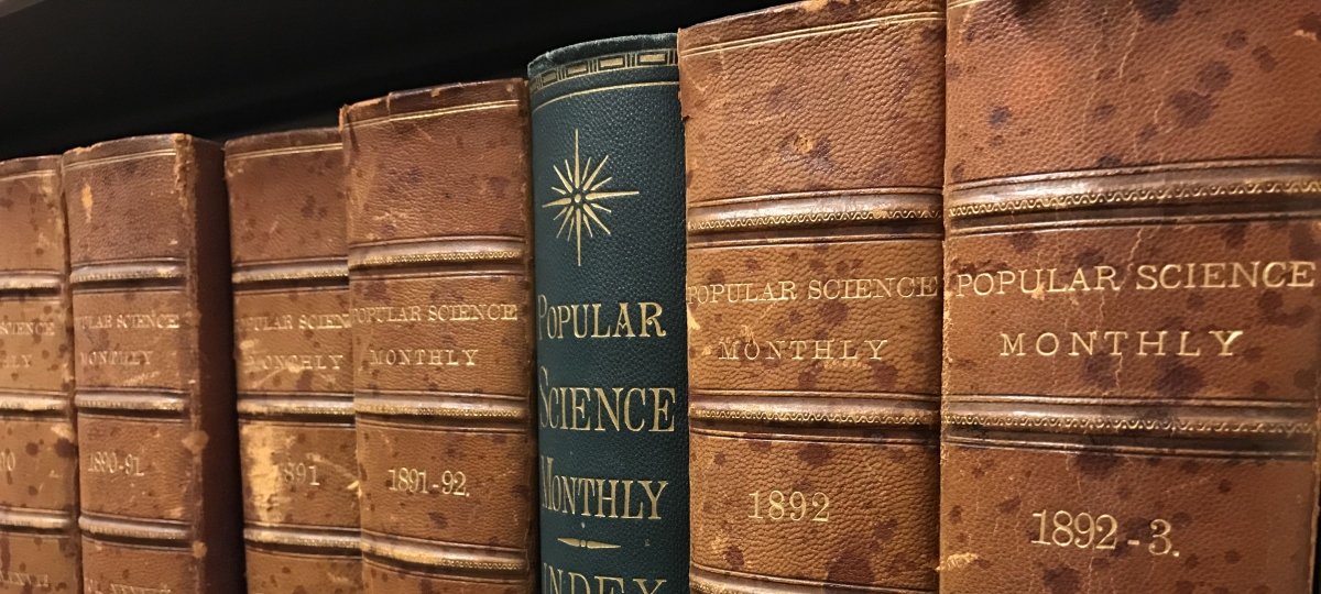 A row of books sit on a shelf, the lettering is faded and reads "Popular Science Monthly". 