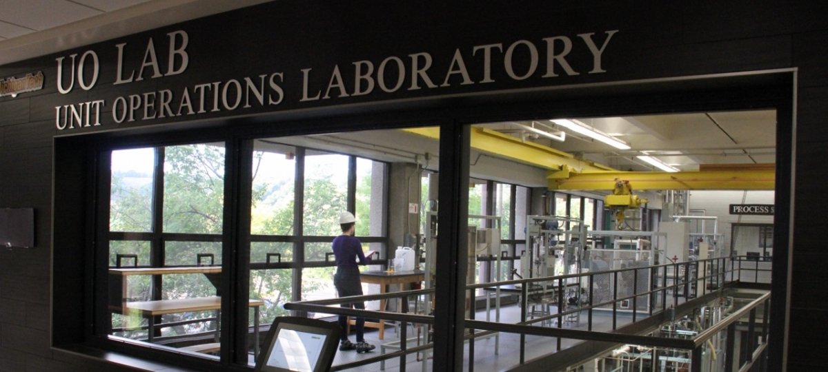 Window into large lab with sign that reads "UO Lab, Unit Operations Laboratory". 