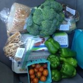 A car seat is piled with orange cherry tomatoes, green peppers, broccoli, bread, dried fruit, eggs, and baked goods.