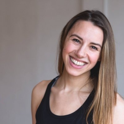 A woman smiles at the camera. She is wearing a black tank top and there is a plain white background.