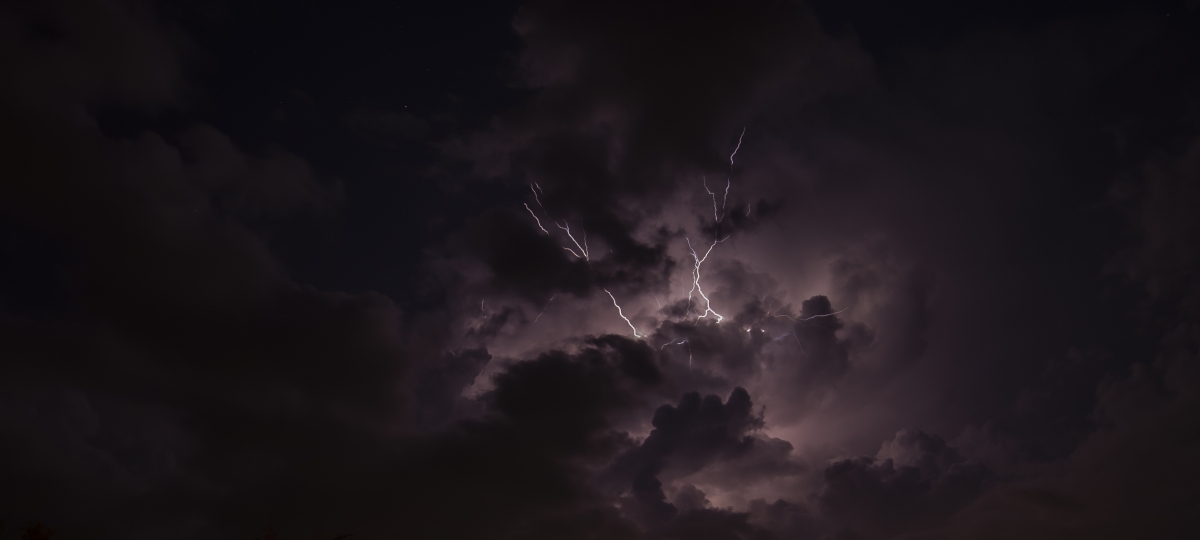 Lightning streaks across the night sky, illuminating the clouds.