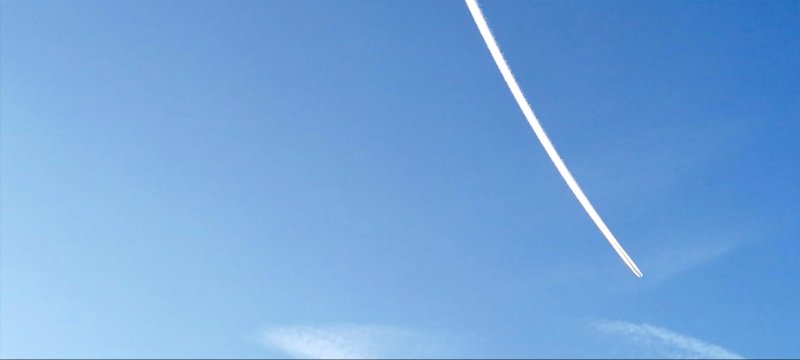 Blue sky with a long white contrail curving through. 