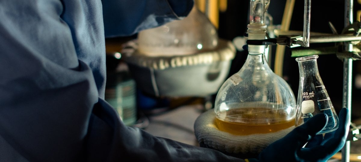 Gloved hands hold a bottle with clear liquid.