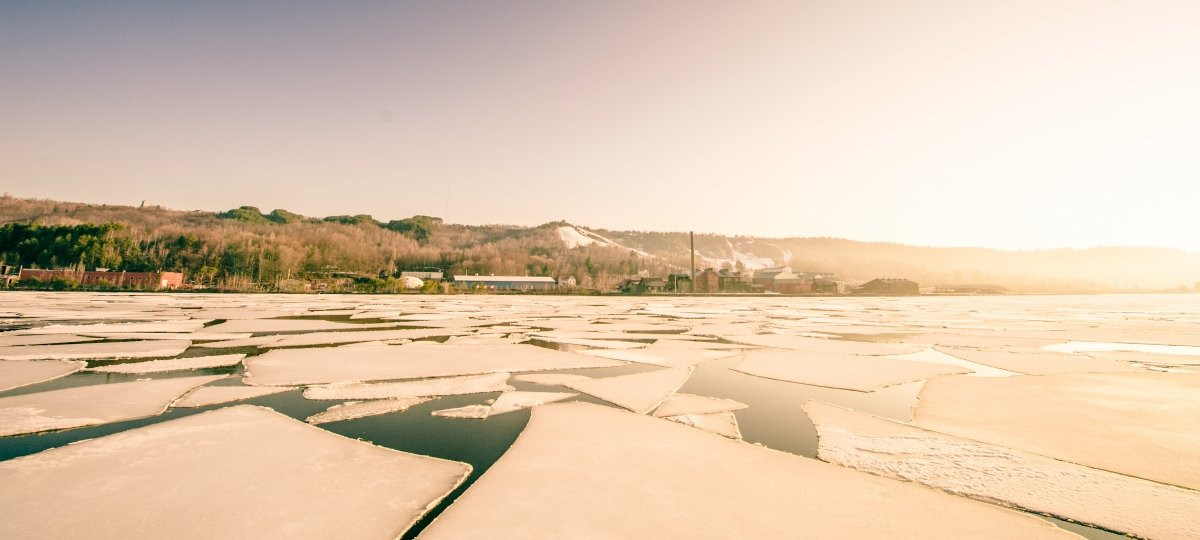 A distant cluster of buildings is lit by bright morning sun with broken ice floes in the foreground.