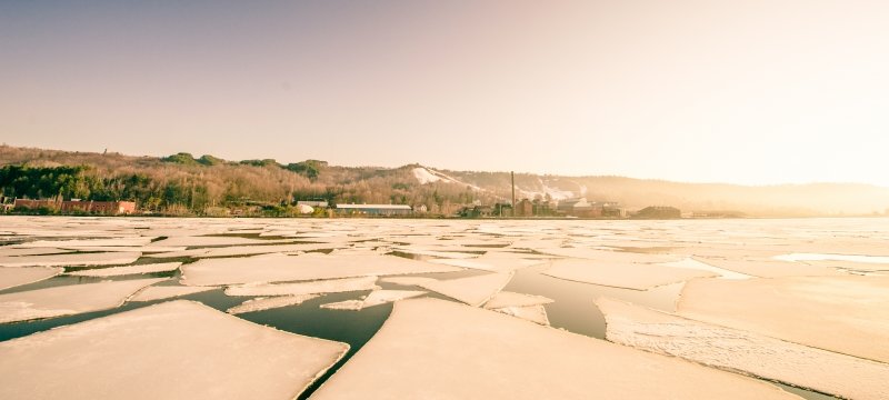 A distant cluster of buildings is lit by bright morning sun with broken ice floes in the foreground. 