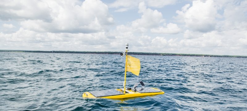 A wave glider in the water, with cliffs and clouds on the horizon.