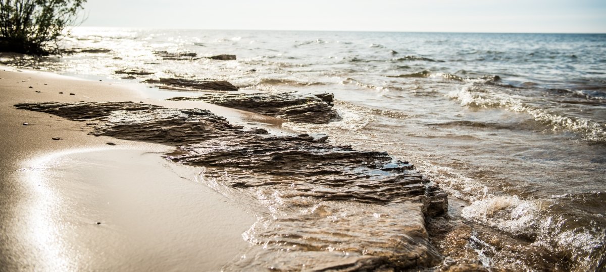 Shore of Lake Superior with bright sunlight, waves, sand, and sandstone.