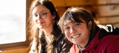 two students smile in the sun painting rocks in a cabin during a nature retreat.