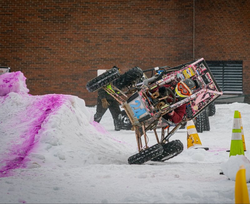 A Baja vehicle laying sidewise on the Winter Invitational Course at Michigan Tech.