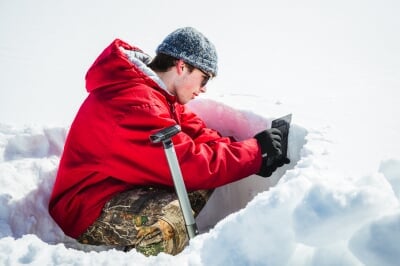 Nathaniel Miller sits in a short snow pit and collects data.