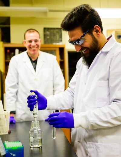 Student using a pipette to take a sample from a bottle while another researcher watches.