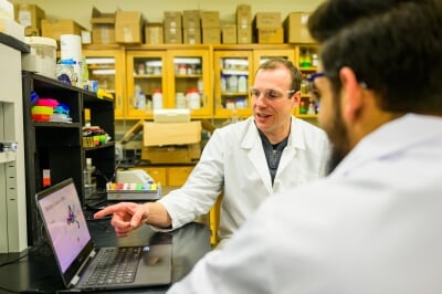 Steve Techtman points at a laptop screen, talking with graduate student researcher.