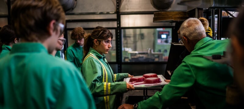 A Summer Youth Program student prepares to cast her fry pan designs, wearing a protective coat and glasses.