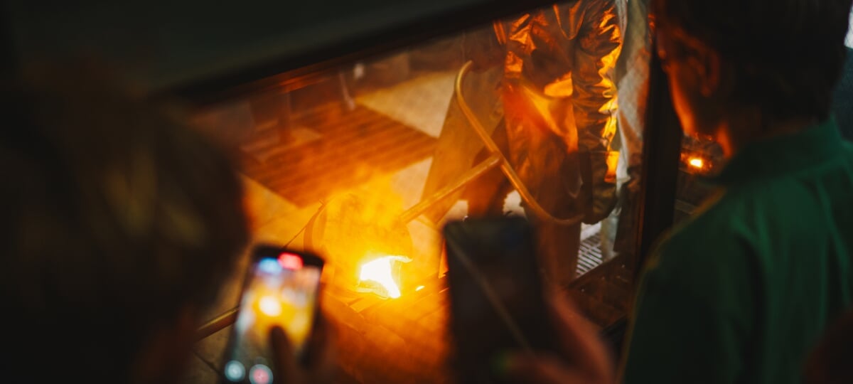 Students watch and record videos from behind protective glass as hot metal is poured into molds at the Michigan Tech foundry.