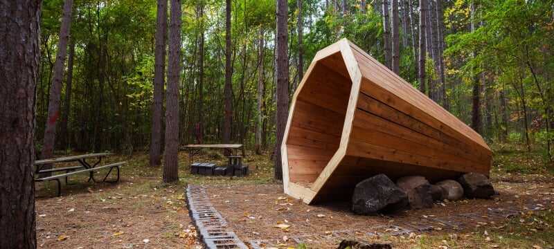 A large conical, megaphone shaped, wooden structure in the woods.