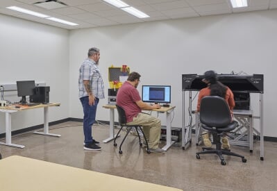 A researcher sits at a computer while a participant wearing a brain-monitoring headset plays the video game Space Trash in a laboratory setting.