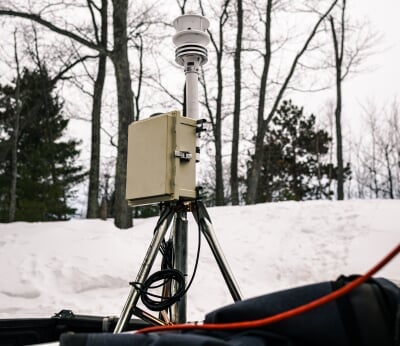 Mounted on a tripod in a truck bed, the isotopic analyzer is a tall, white piece of equipment with an electrical box attached to it, standing approximately three feet over the truck bed with many cables.