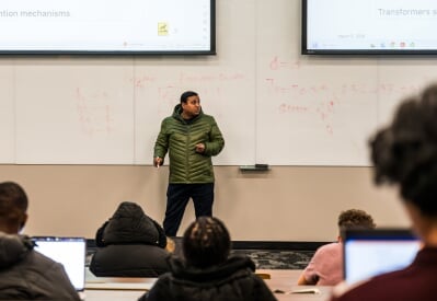 Sujan Kumar Roy stands in front of a large lecture hall while students take notes on laptops..