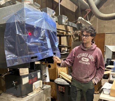 Aidan Bustos stands next to a hydraulic machine press.