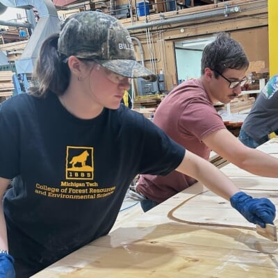 Emily Costigan works in the U. J. Noblet Forestry Building wood lab, applying a treatment to lumber alongside another student.