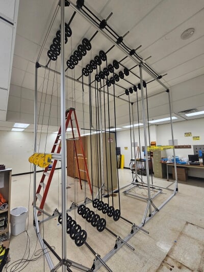 Large mechanical apparatus with multiple black pulleys and cables arranged vertically inside a spacious industrial room.