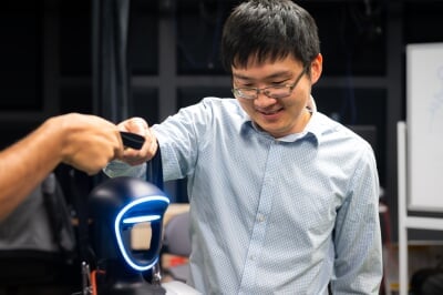 Tan Chen in a light blue shirt interacting with a robot by scanning a device near its illuminated face panel.