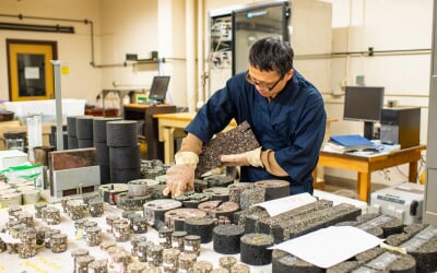 Zhanping You examining cylindrical core samples of asphalt and concrete in a laboratory setting with testing equipment.