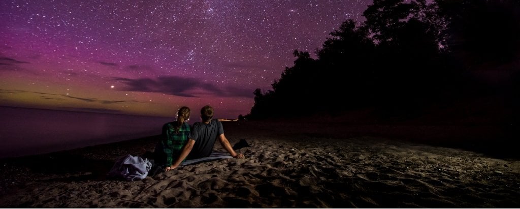 Two people sitting under a purple night sky full of stars.