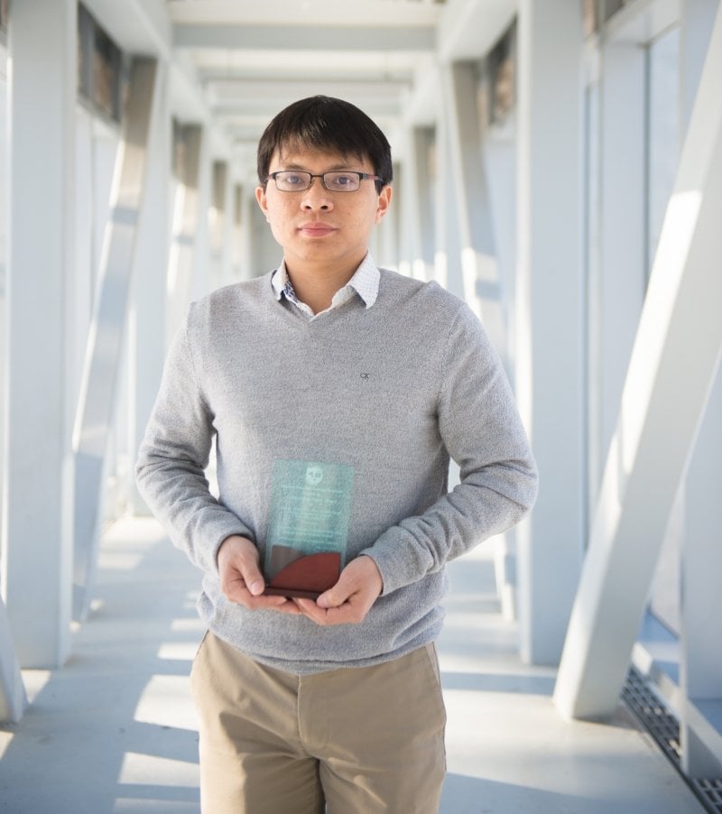 A man wearing glasses holds a glass award plaque.