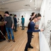 Students work on their drawings on the studio wall while others observe.