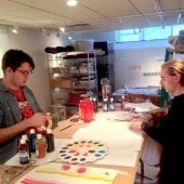 One student typing a canvas, the other student moving art papers at a workbench