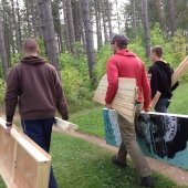 Three students walking along the Tech Trails, carrying lumber and a People's Climate March poster.