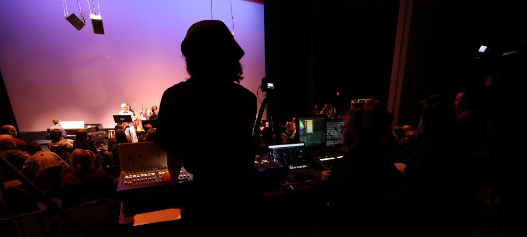 Student at sound board looking at jazz band on stage