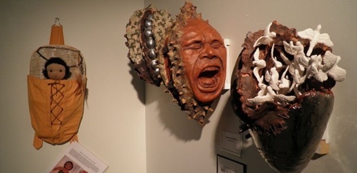 Art created by students displayed in the gallery. Masks of expressioned faces, one screaming, and an example of a native american baby carrier.