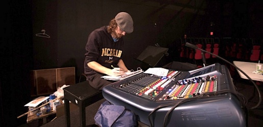 Student sitting, writing, at a sound board inside McArdle Theatre.