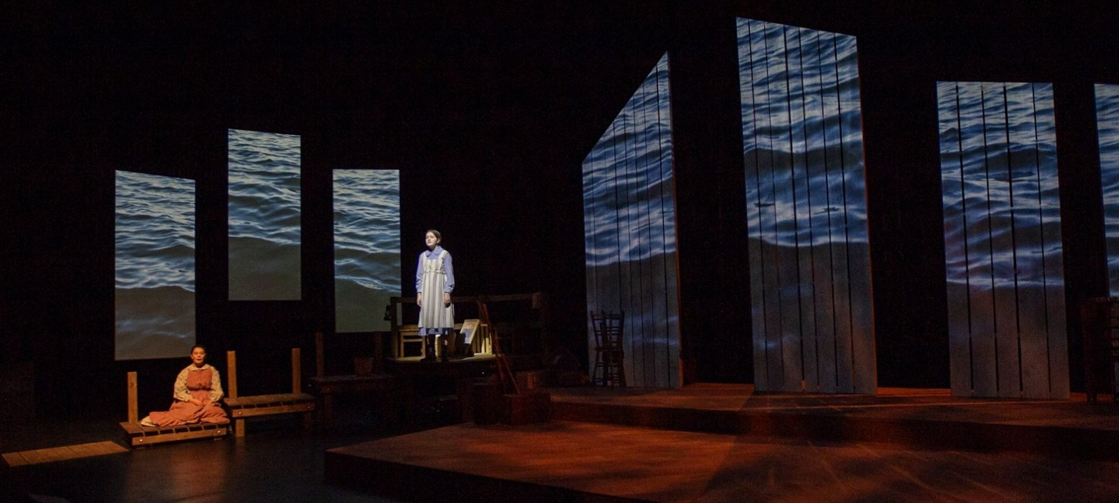 Students acting on stage, one on a higher platform another on a lower platform.