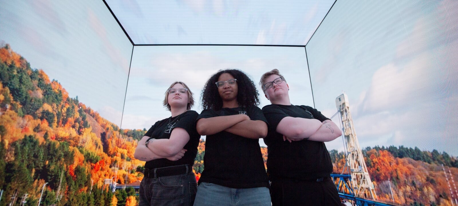 Three students stand inside an LED wall cube with photos of the Keweenaw Portage