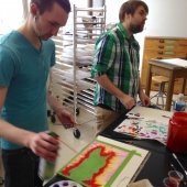 Two art students standing and painting with one student holding an air sprayer.