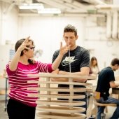 Faculty explains as a student looks at a multi-tiered, round, wooden project.