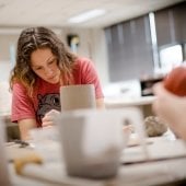 Student sits a workbench working on a piece of pottery.