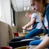 Students sit at pottery wheels working clay.