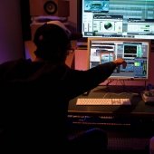 Two students sitting at the sound board and monitor with one pointing at the screen.