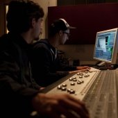 Two students sitting at the sound board and monitor adjusting controls.