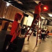 Technician on a ladder inside the Lighting and Sound Lab talking to a student below.