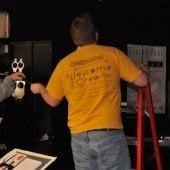 One student standing on a ladder looking up while another student hands lighting film.